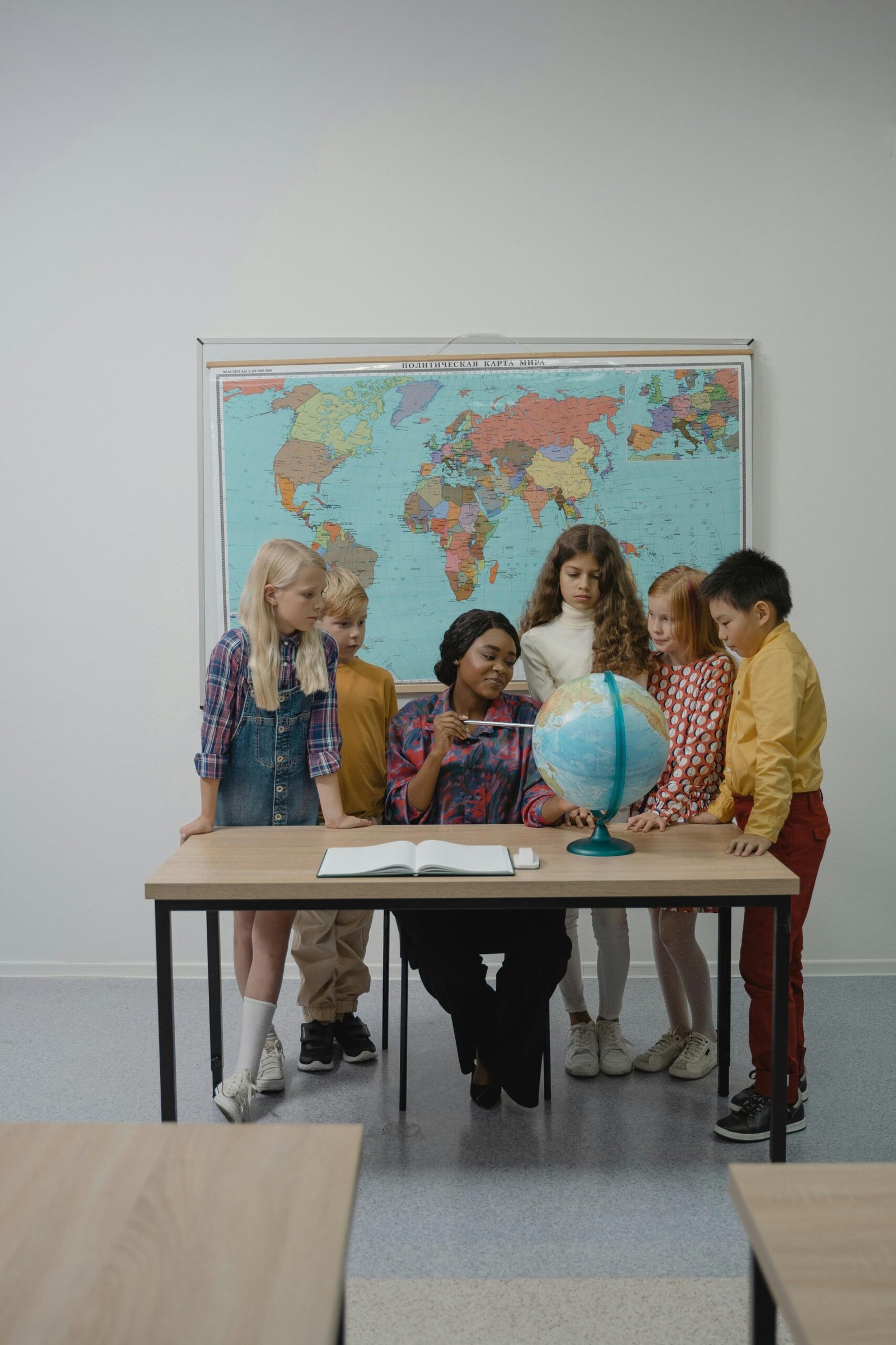 A teacher and students learning geography with a globe in the classroom.